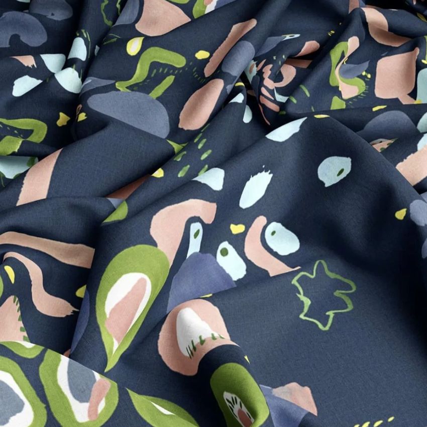 Closeup of cotton fabric mockup featuring an abstract pattern in green, pink, and white on a dark blue background, with visible folds.