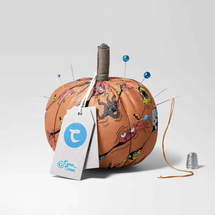 Fabric pumpkin mockup decorated with colorful monster illustrations, pins, and a thread, set on a light gray background.