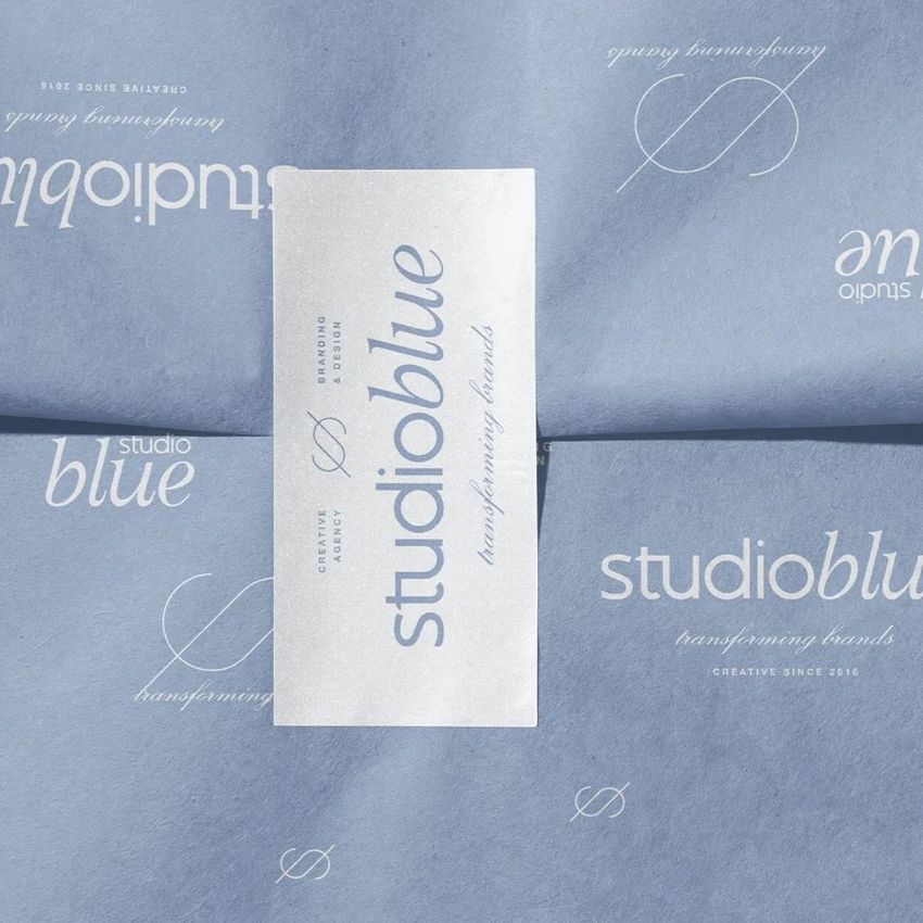 Sticker mockup featuring a rectangular white sticker with blue text placed on folded blue tissue paper with elegant script patterns.