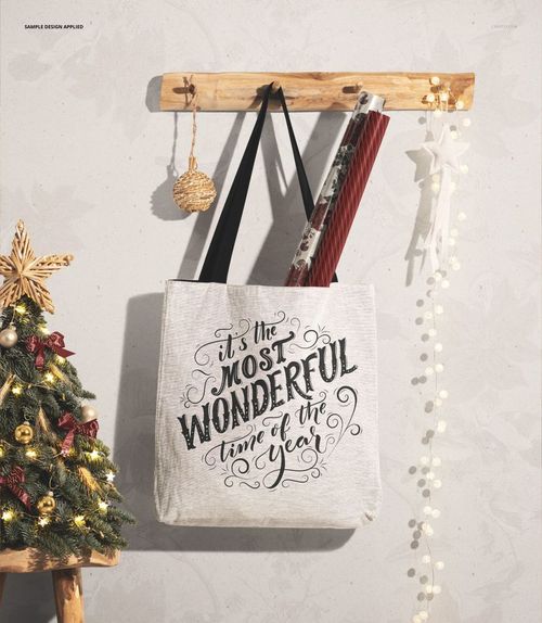 Christmas woven tote bag mockup displayed on a wall hook, with festive ornaments and rolled wrapping paper inside.