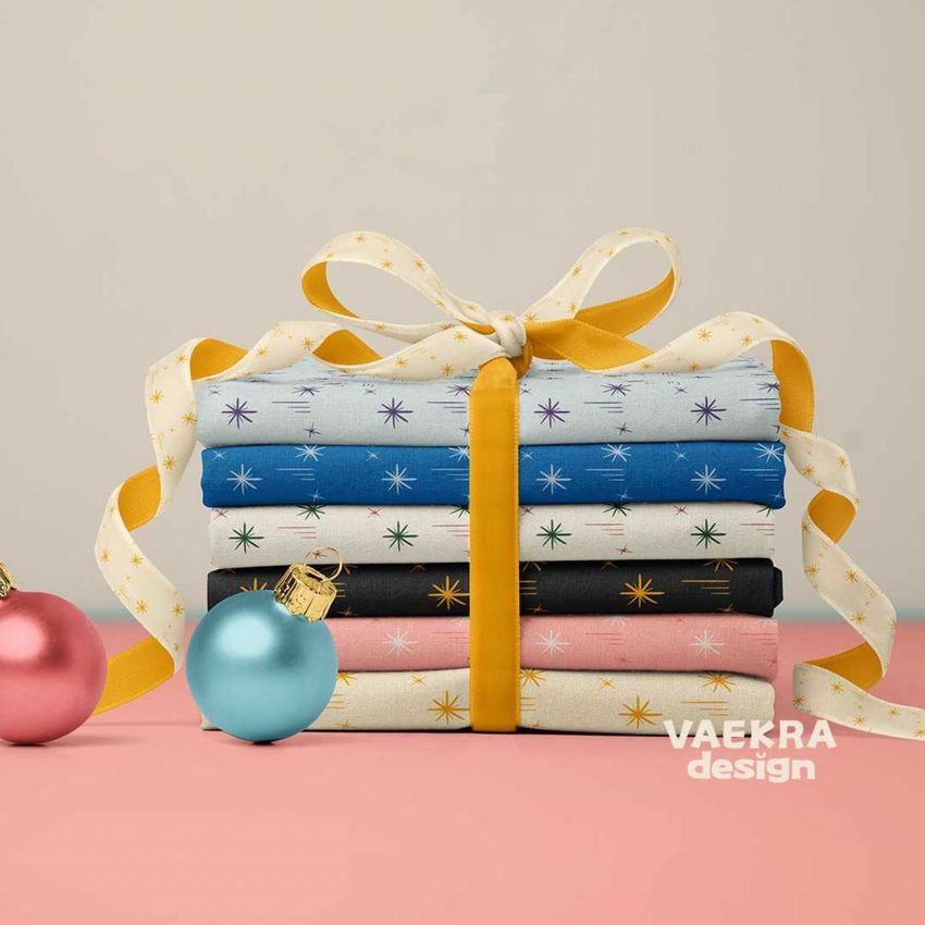 Fabric stack mockup featuring folded textiles with star patterns, tied with a yellow ribbon, and Christmas baubles on a pink surface.