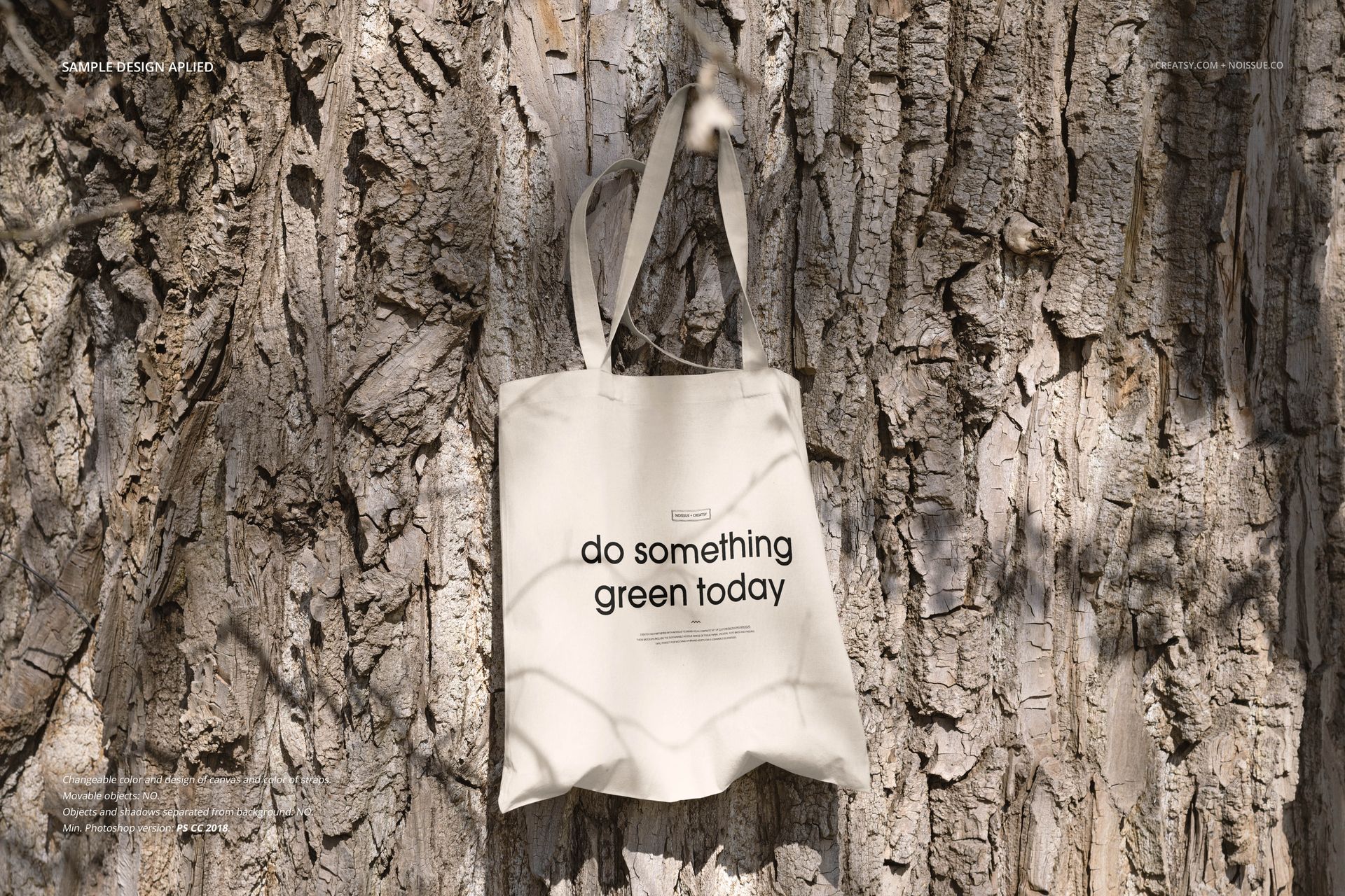 Cream-colored tote bag mockup hanging against textured tree bark, front view showing simple text design.
