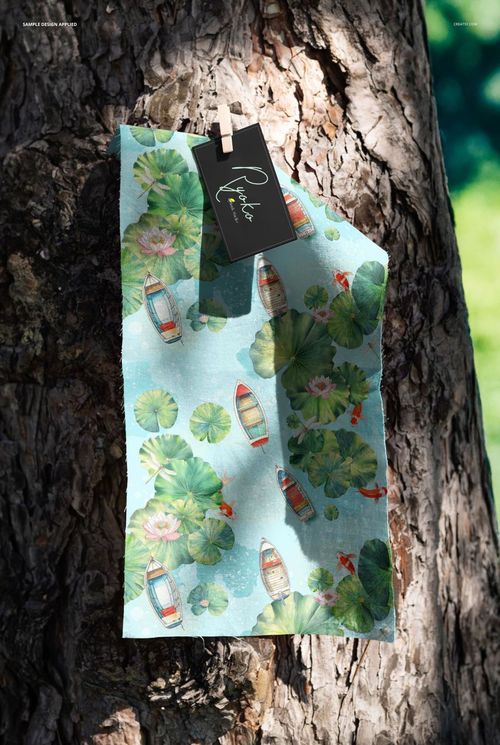 PSD mockup of a fabric swatch decorated with aquatic motifs, secured to a textured tree trunk in a sunlit setting.