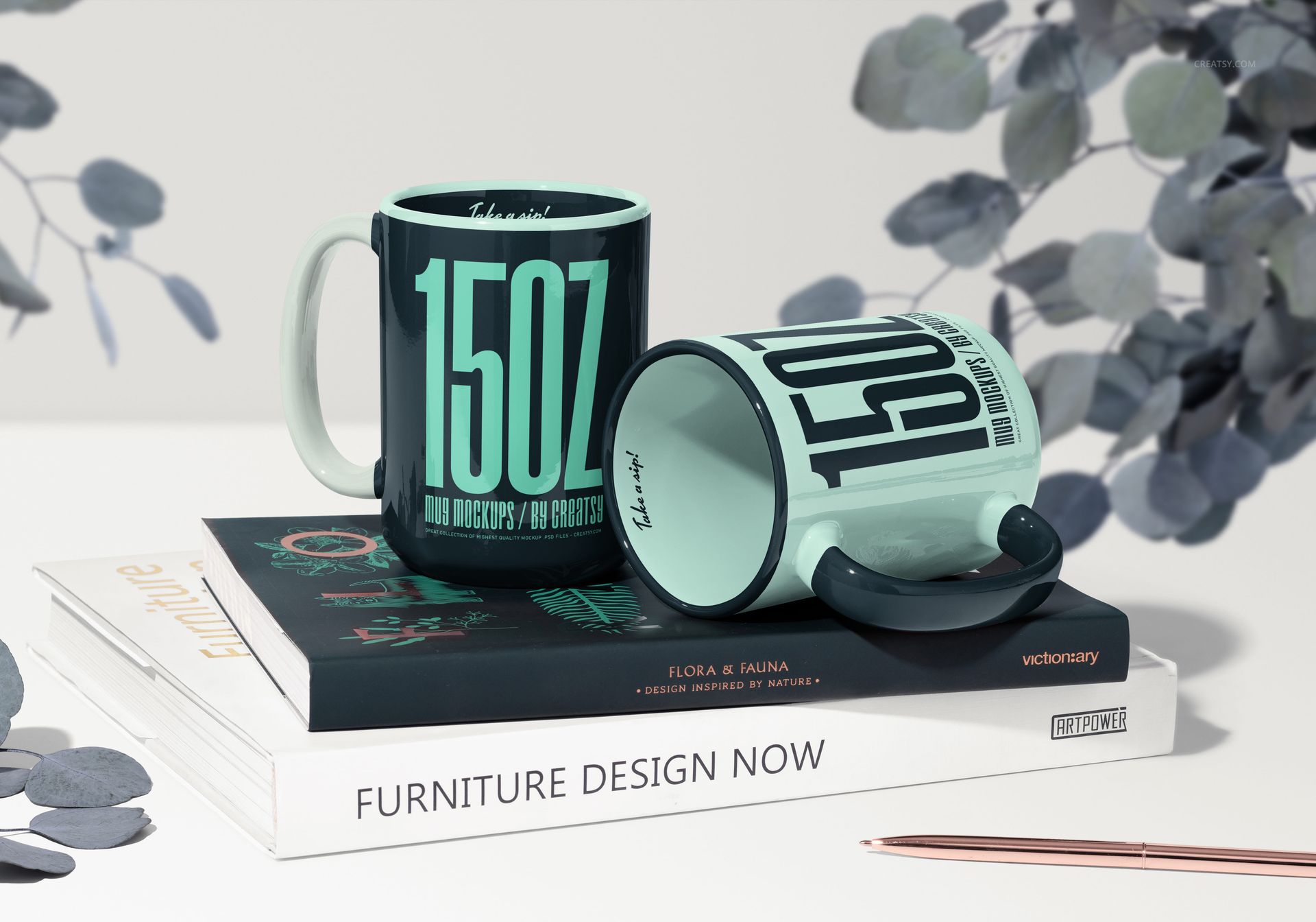 Mockup of two large mugs in mint green with bold black lettering, displayed on books with a pen and decorative leaves.