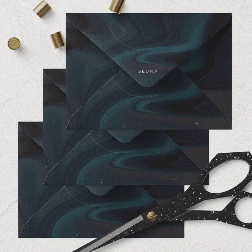 C6 envelope mockup featuring three dark envelopes with a marbled pattern, arranged on a light textured surface with scissors and brass fasteners.
