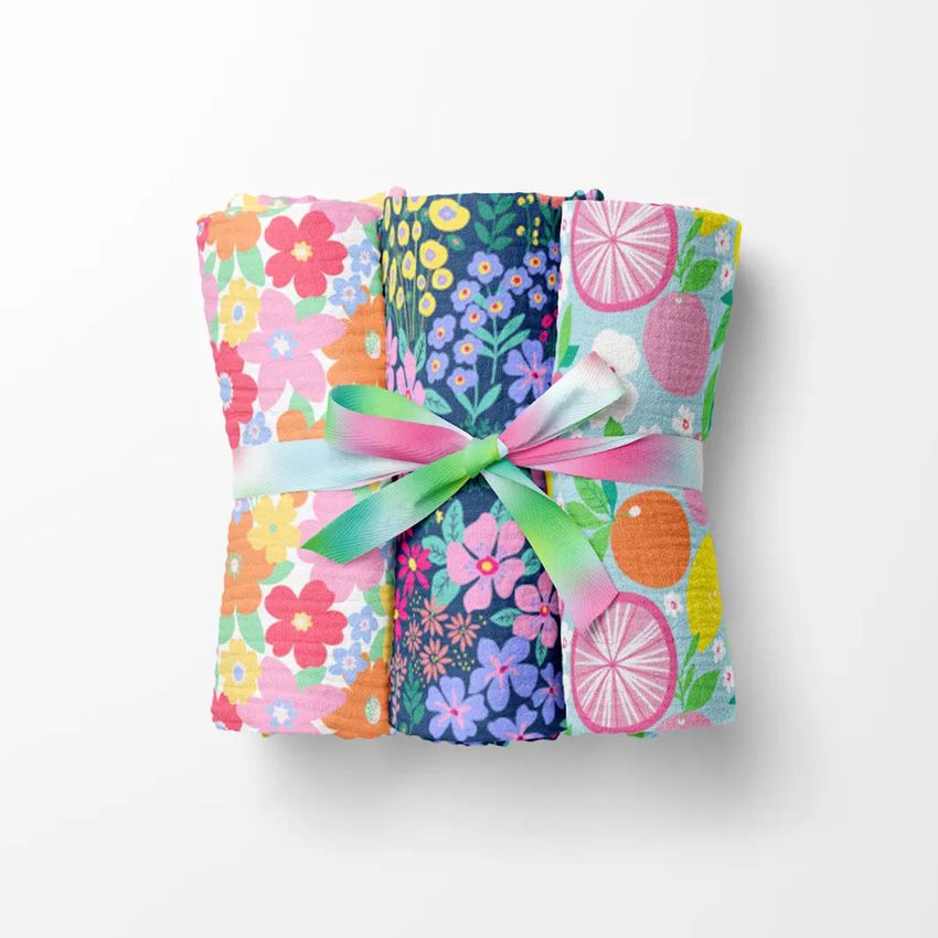 Crinkle muslin swaddle blanket mockup featuring three folded blankets with colorful floral and fruit patterns tied with a pastel ribbon.