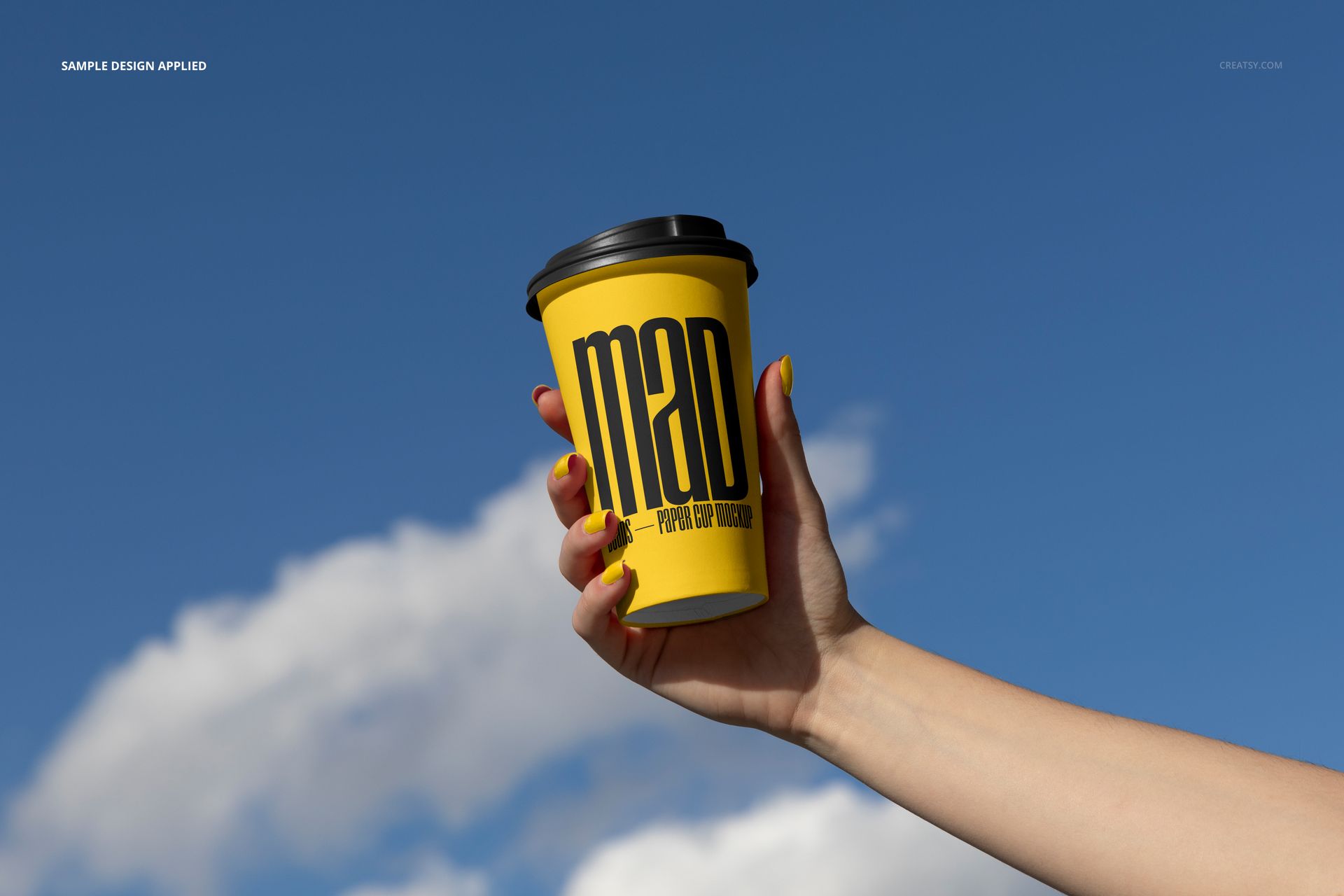 Yellow paper cup mockup with black lid and large black lettering, held up in front of a bright sky with clouds.