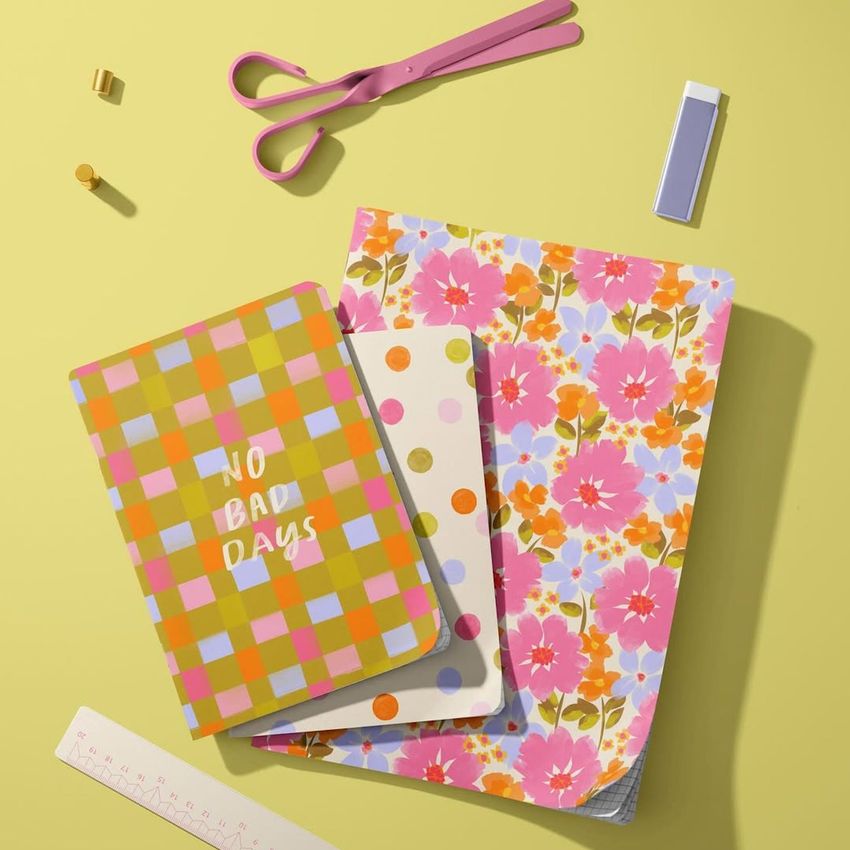 Stationery mockup scene showing three notebooks arranged on a yellow surface with scissors, a ruler, and small desk items.