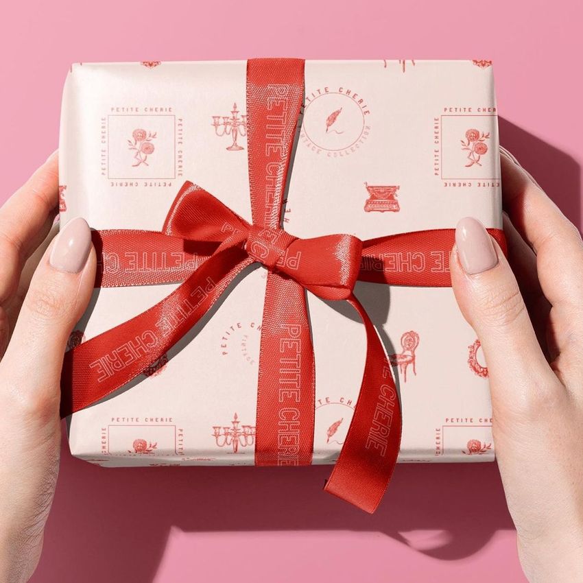 Square packaging mockup with patterned pink wrapping paper and a red bow, shown from above on a solid pink surface.
