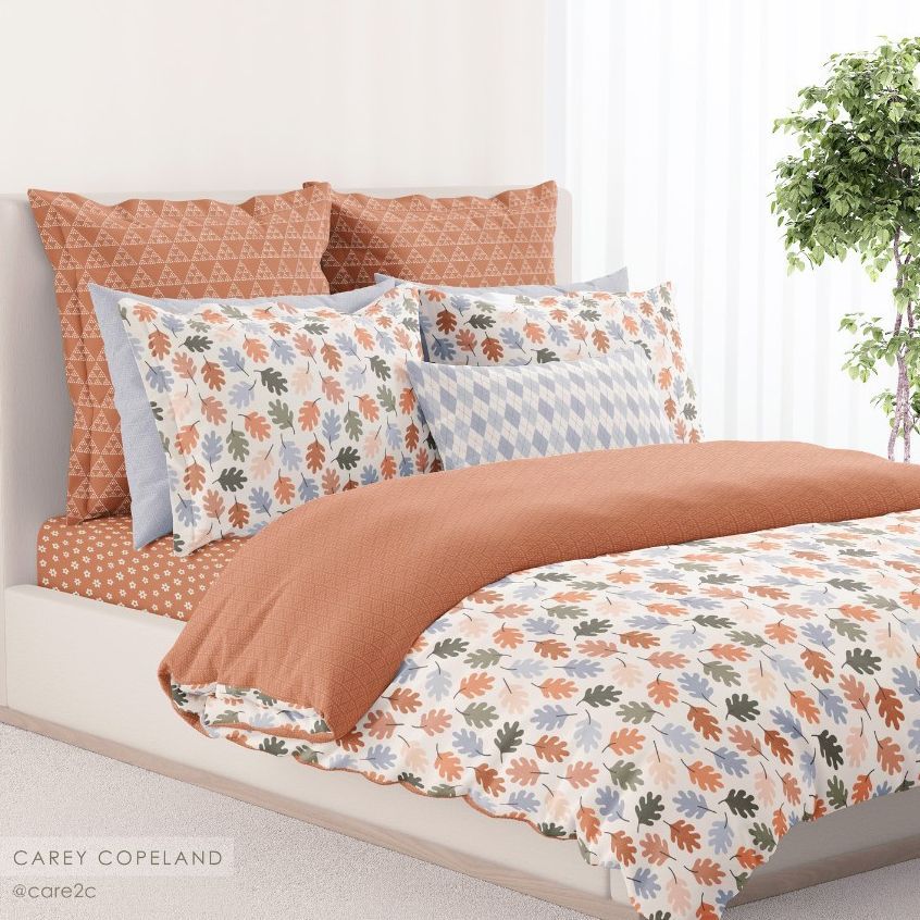 Bedding mockup featuring a neatly made bed with patterned pillows and duvet in autumn leaf and geometric prints, set in a bright bedroom.