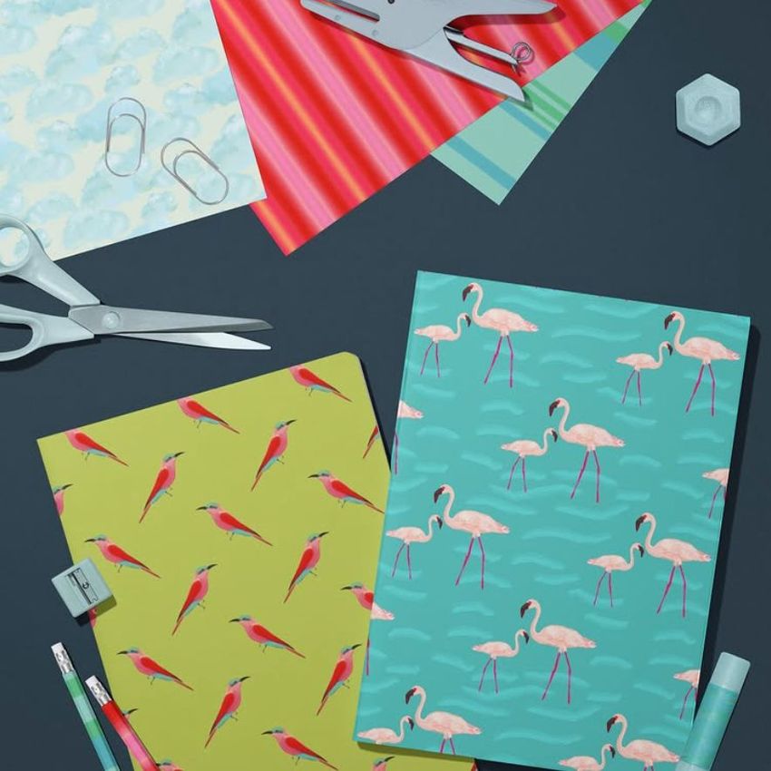 Stationery mockup featuring two A4 notebooks with bird patterns, surrounded by scissors, paper clips, and pencils on a dark surface.