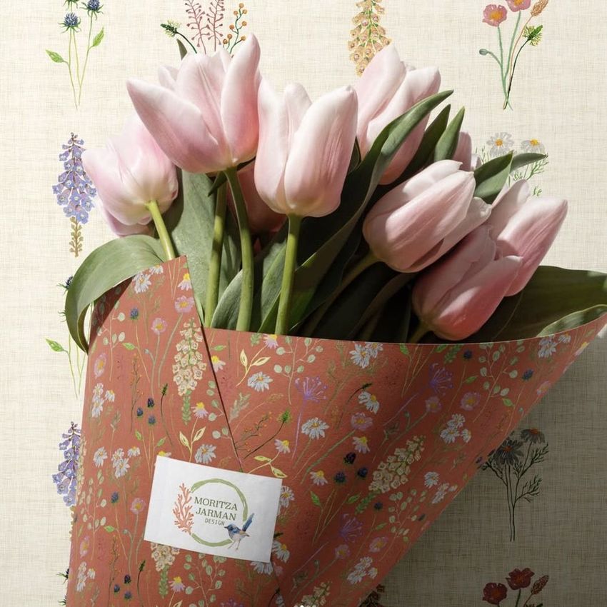 Flower packaging cone mockup with pink tulips, wrapped in floral-patterned paper against a cream wall with botanical illustrations.