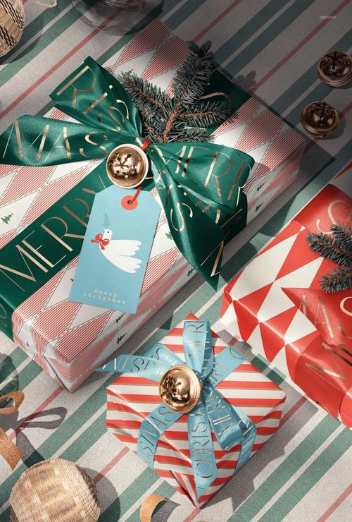 Christmas gift boxes wrapped in patterned paper with festive ribbons and tags, viewed from above on a striped surface.