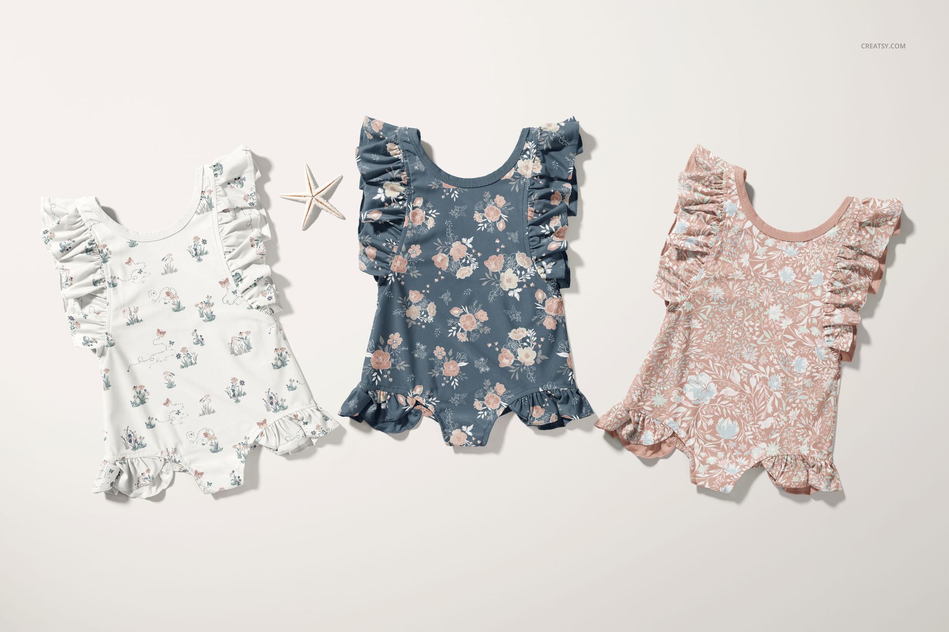 PSD mockup of baby ruffle swimsuits featuring soft floral designs in white, blue, and pink, shown from a top view.