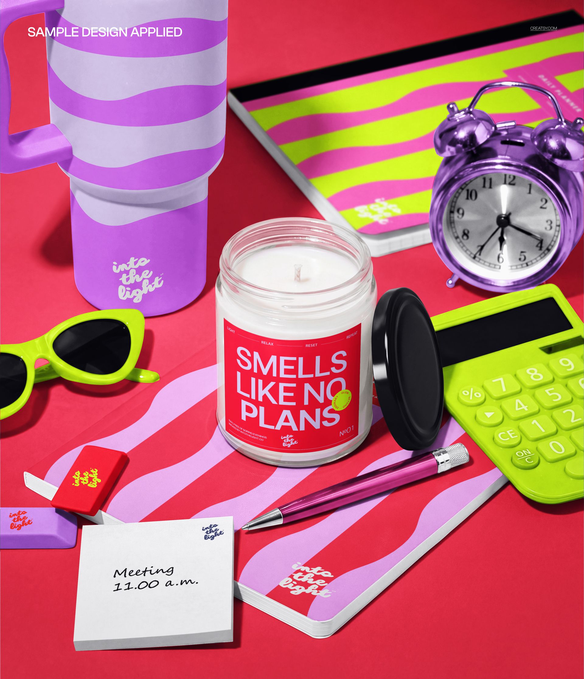 PSD mockup of a scented candle in a glass jar placed among notebooks, sunglasses, pen, and desk items in bright colors.