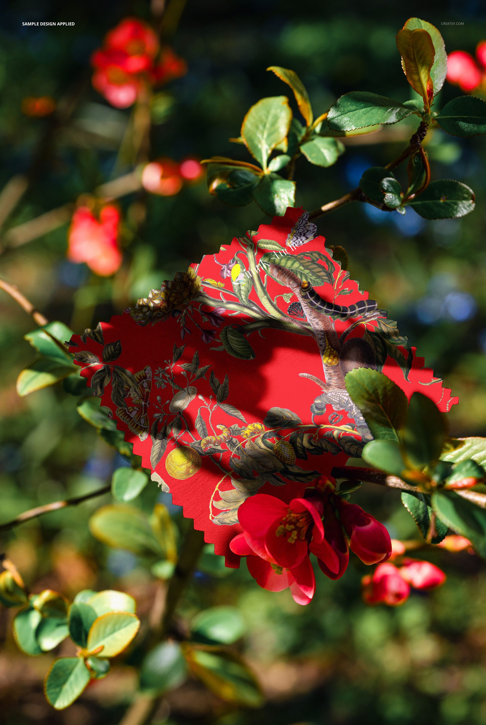 PSD mockup showing a square fabric swatch with colorful floral motifs placed among branches and vibrant red blossoms.