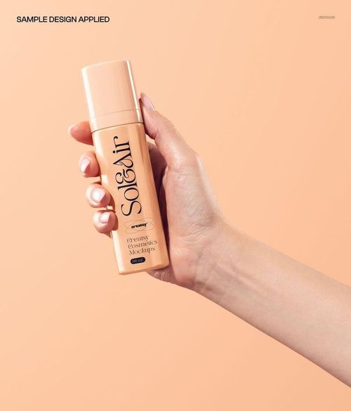Hand holding a cylindrical cosmetic bottle with a beige label on a light peach background, front view mockup.