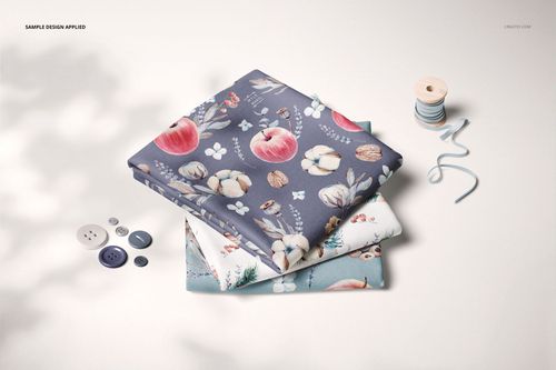 Folded fabric PSD mockup set showing three patterned textiles, surrounded by sewing accessories and soft shadows.