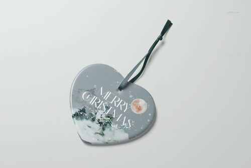 Christmas ornament mockup in heart shape, decorated with a forest and moon illustration, lying flat with attached ribbon.