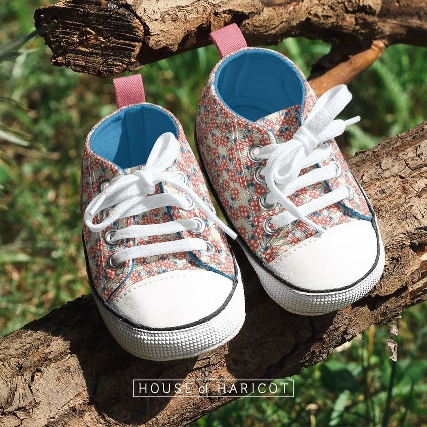 Baby sneakers mockup featuring a pair of patterned shoes with white laces and blue interiors, placed on tree branches outdoors.