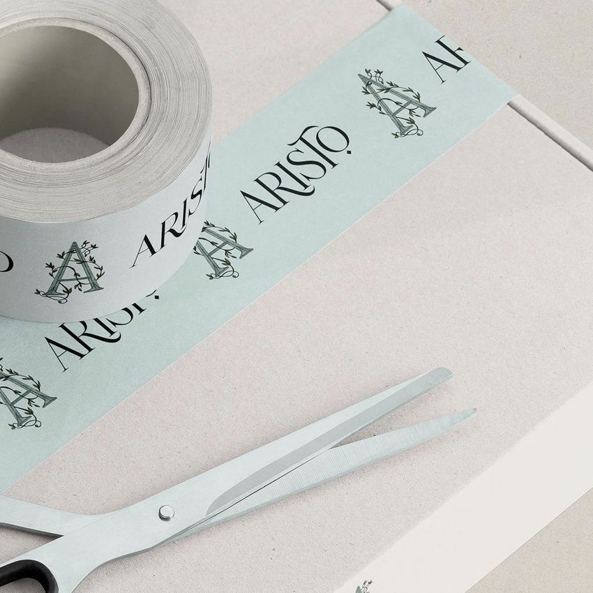 Mailing box mockup with a roll of branded tape and a pair of scissors on a light beige surface, viewed from above.