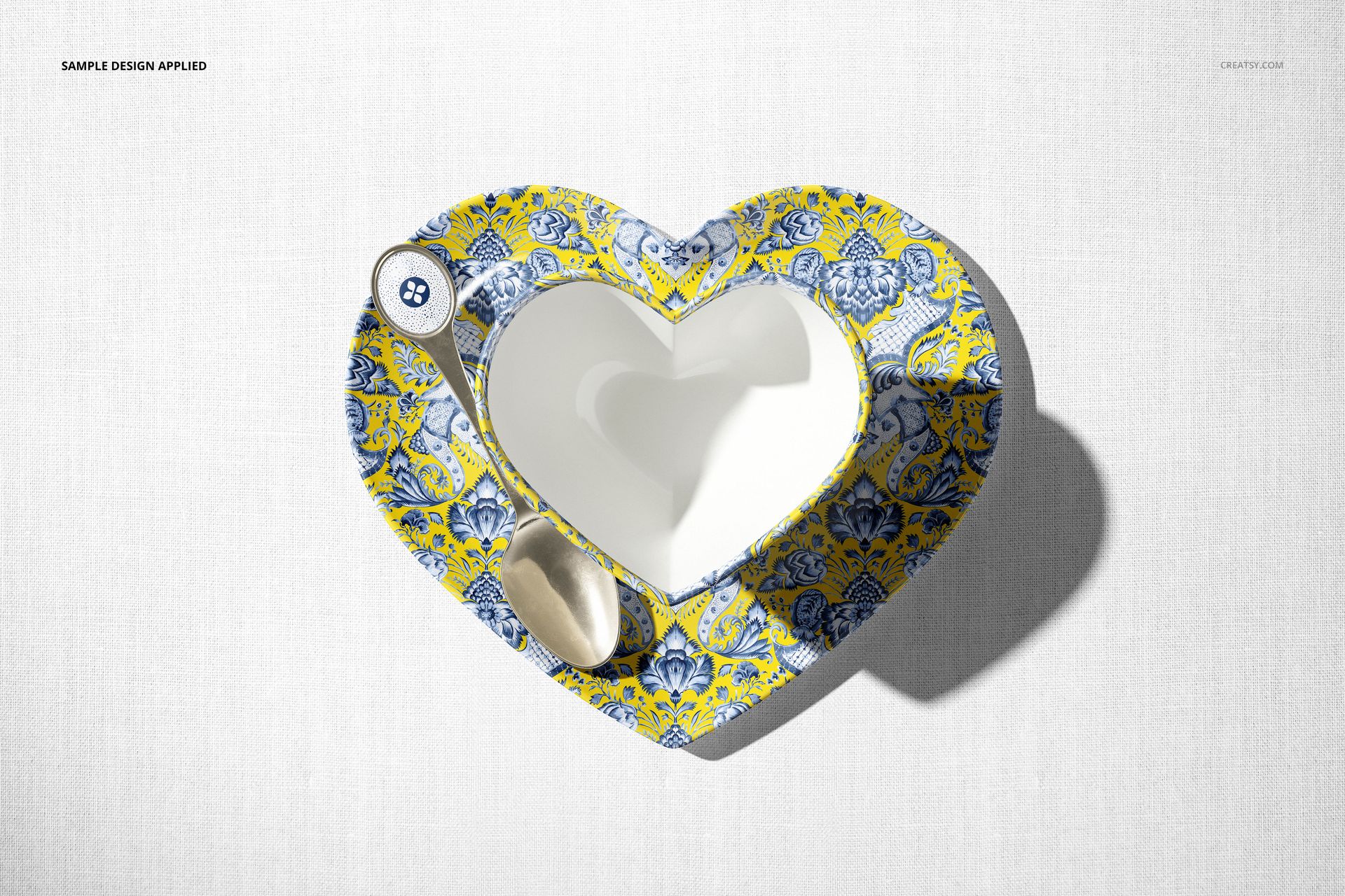Heart-shaped cup mockup on a patterned saucer with metallic spoon, shown from above against a light background.