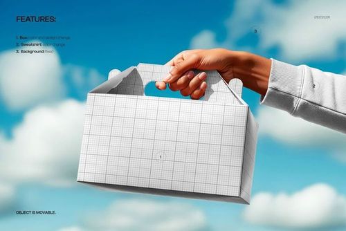 Close-up of a person’s hand gripping a blank gable box mockup with grid lines, sky and clouds in the background.