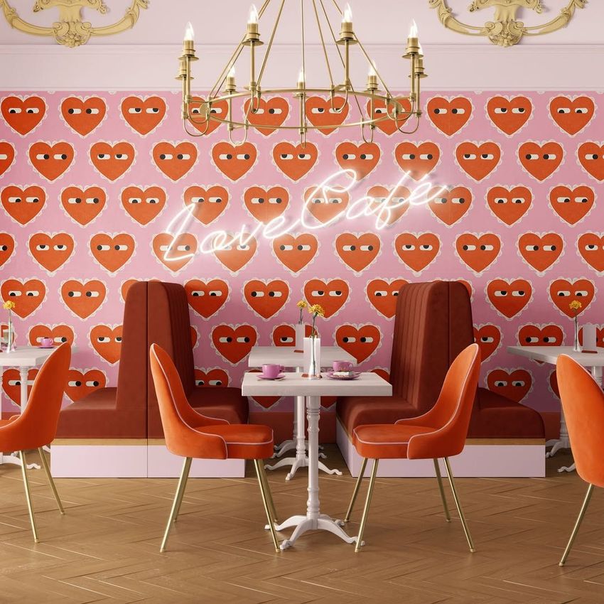 Cafe interior wallpaper mockup featuring a pink wall with a repeating red heart pattern, orange chairs, and a gold chandelier.