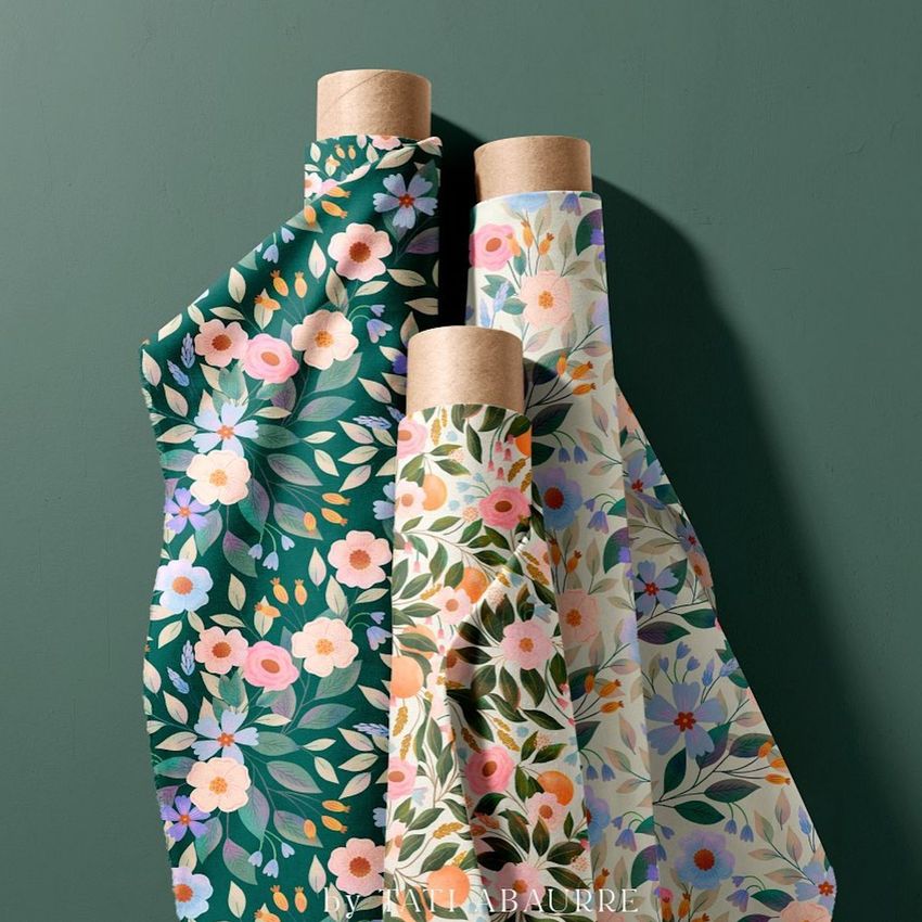 Three fabric rolls mockup featuring floral patterns in green, blush pink, and cream tones, arranged upright against a green wall.