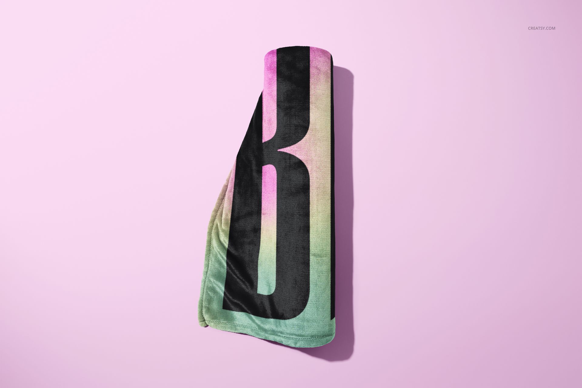 Fleece blanket mockup featuring bold black typography over a soft green and pink gradient, shown rolled up.