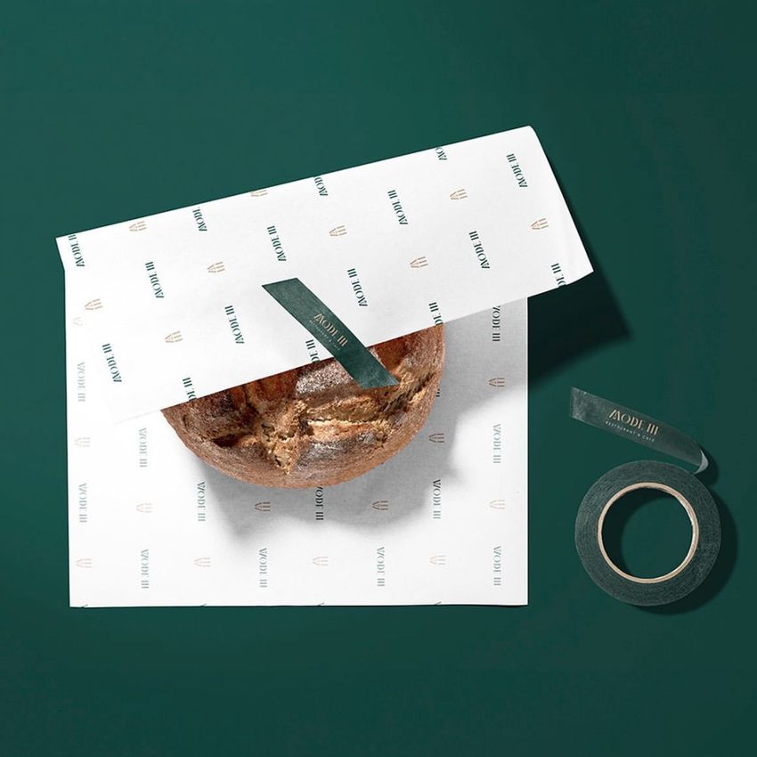 Food safe paper mockup featuring a round loaf of bread partially wrapped in white patterned paper with green tape on a green background.
