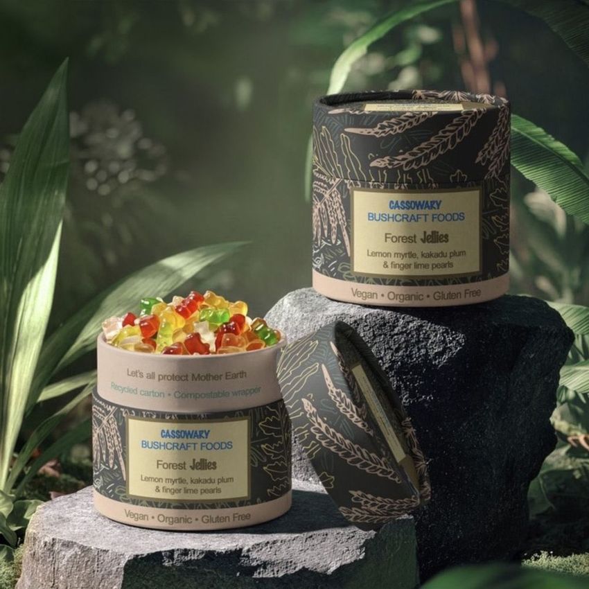 Paper tubes packaging mockup for food products displayed outdoors on stone, with leafy jungle background and colorful jellies inside.