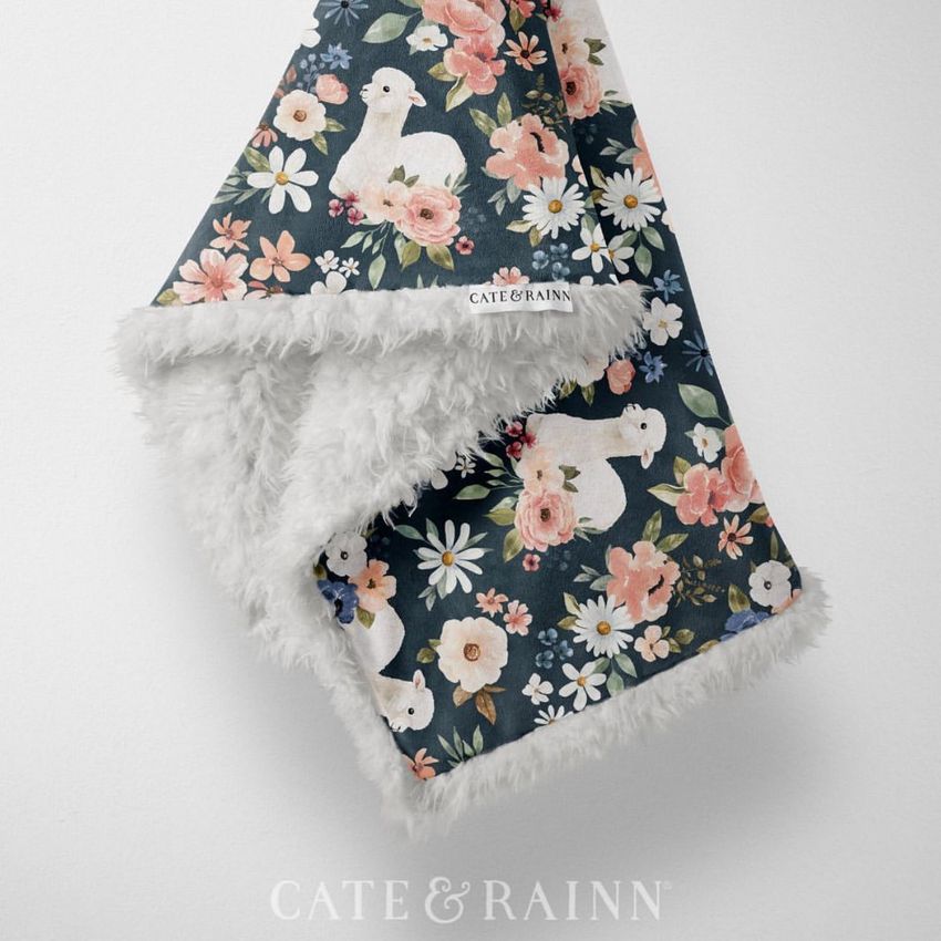 Sherpa baby blanket mockup featuring a floral and llama pattern on a dark background, draped to show soft white fleece.