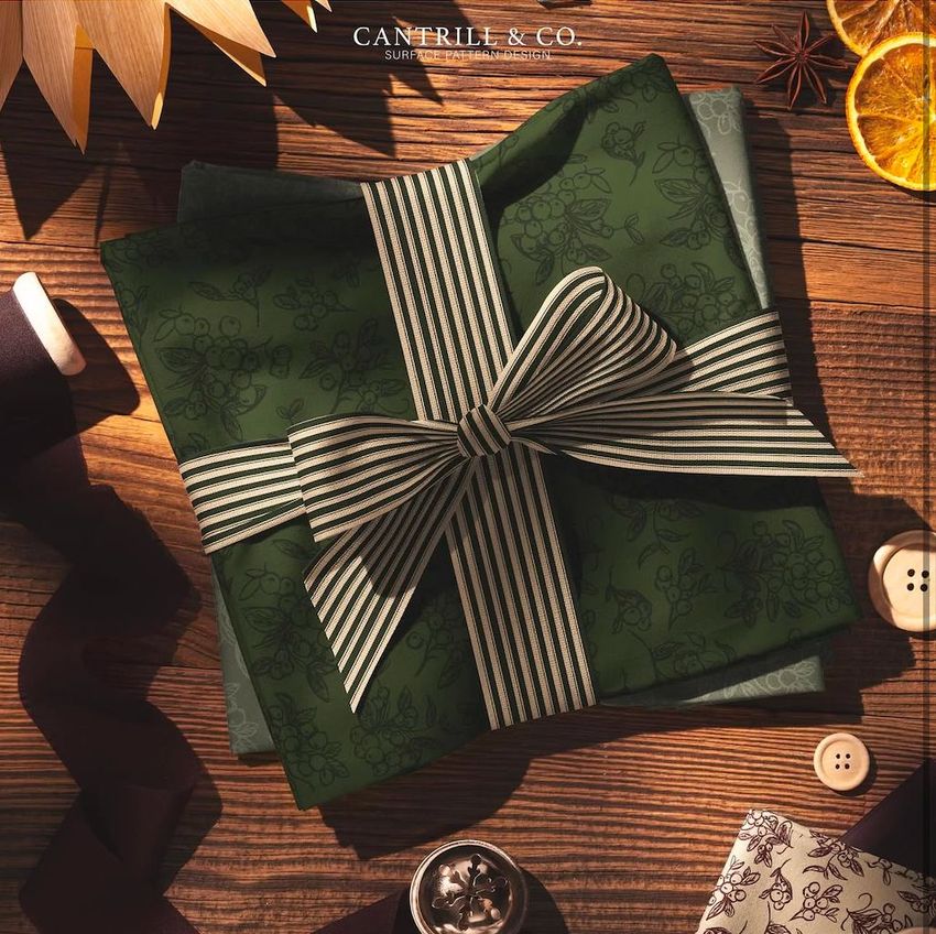 Christmas folded cotton fabrics mockup featuring green fabric with a berry motif, tied with a striped ribbon on a rustic wooden table.