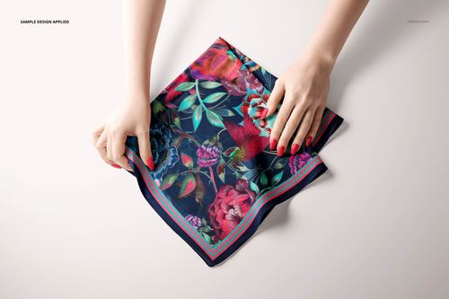 Top view of a square silk scarf mockup featuring colorful flowers, with hands holding the edges on a plain background.