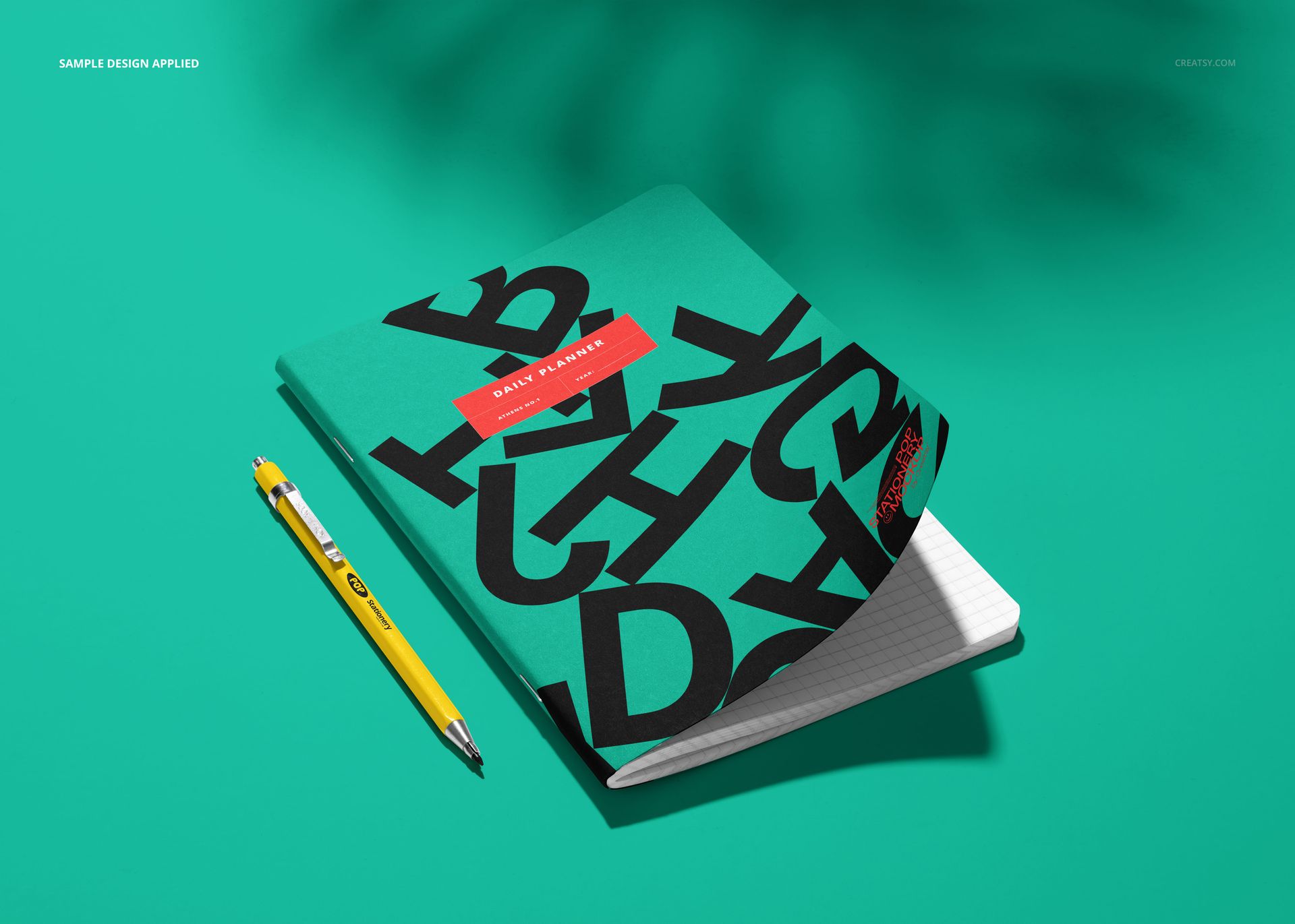 Notebook mockup with a raised corner, featuring a green cover with black letters and a yellow pen beside it.