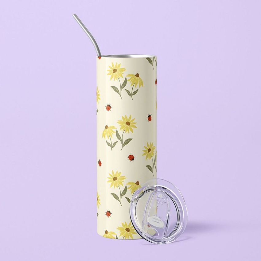 20oz skinny tumbler mockup featuring a floral and ladybug pattern on a light background, with a metal straw and clear lid, set against a pastel purple surface.
