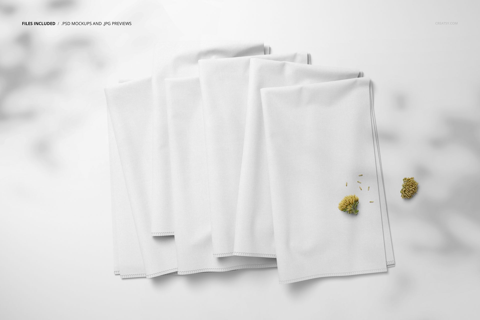 Fabric stack mockup showing multiple white cloths folded together on a light background, top perspective with floral props.