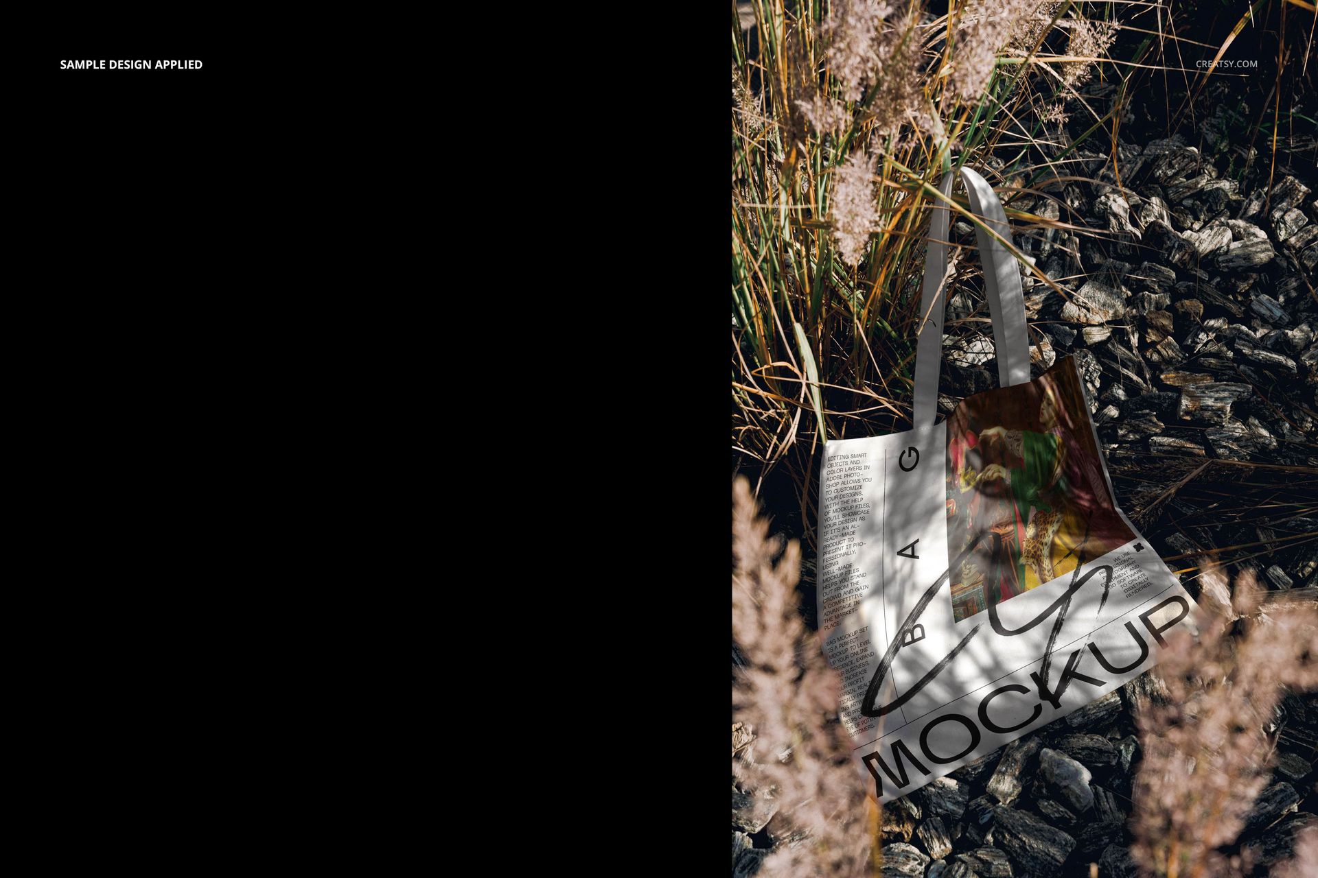 Tote bag mockup resting on dark rocks among tall dry grass, featuring white handles and a customizable design area.