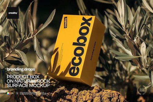 Rectangular yellow product box mockup resting on a natural rock surface surrounded by green leaves.