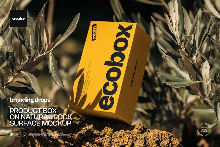 Rectangular yellow product box mockup resting on a natural rock surface surrounded by green leaves.