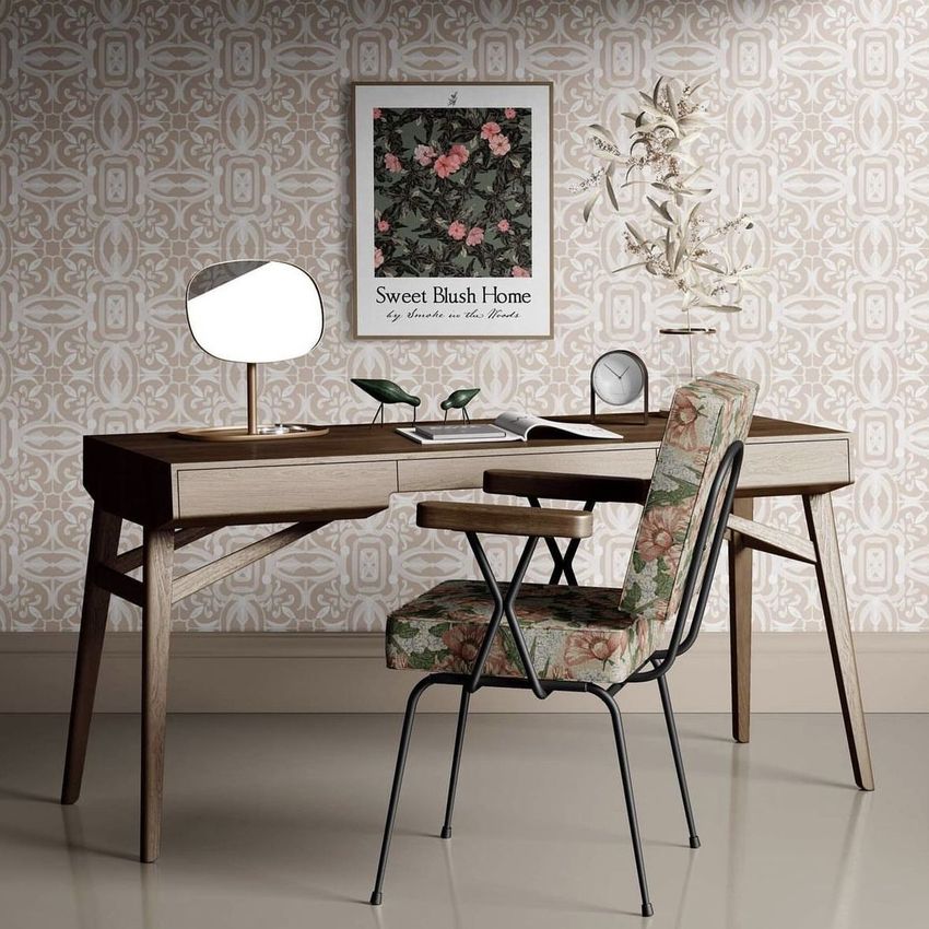 Interior scene with a wooden desk and floral upholstered chair, featuring a framed poster mockup on a patterned wallpapered wall.