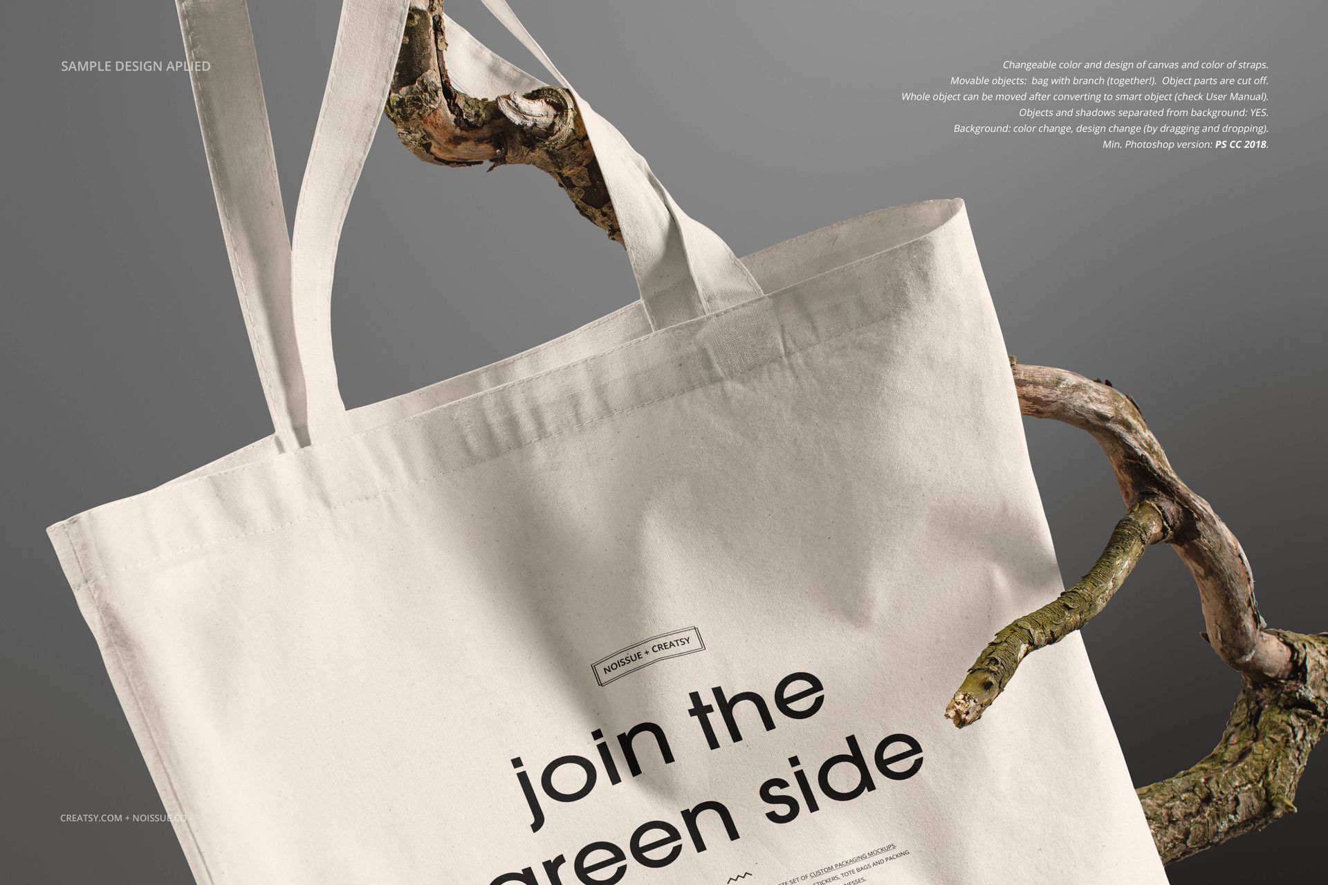 Front view of a plain white tote bag mockup hanging from a tree branch, with black text design on the fabric.