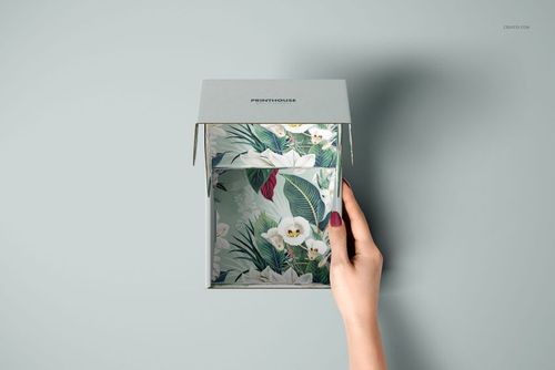 Open mailer box mockup featuring tropical floral design on the interior, shown from above with a hand lifting the lid.
