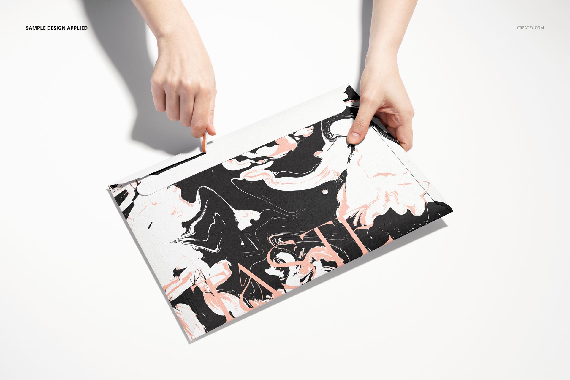 Top view of a tear strip envelope mockup featuring swirling black, white, and peach colors, held by two hands.