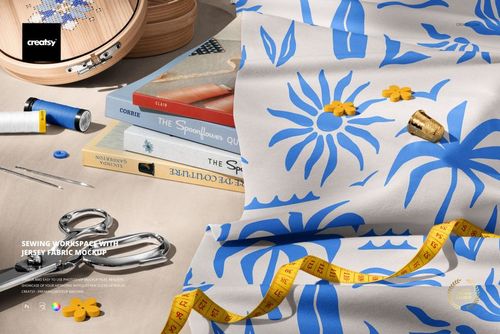 Jersey fabric mockup with blue flower design displayed on a desk surrounded by sewing supplies and books.