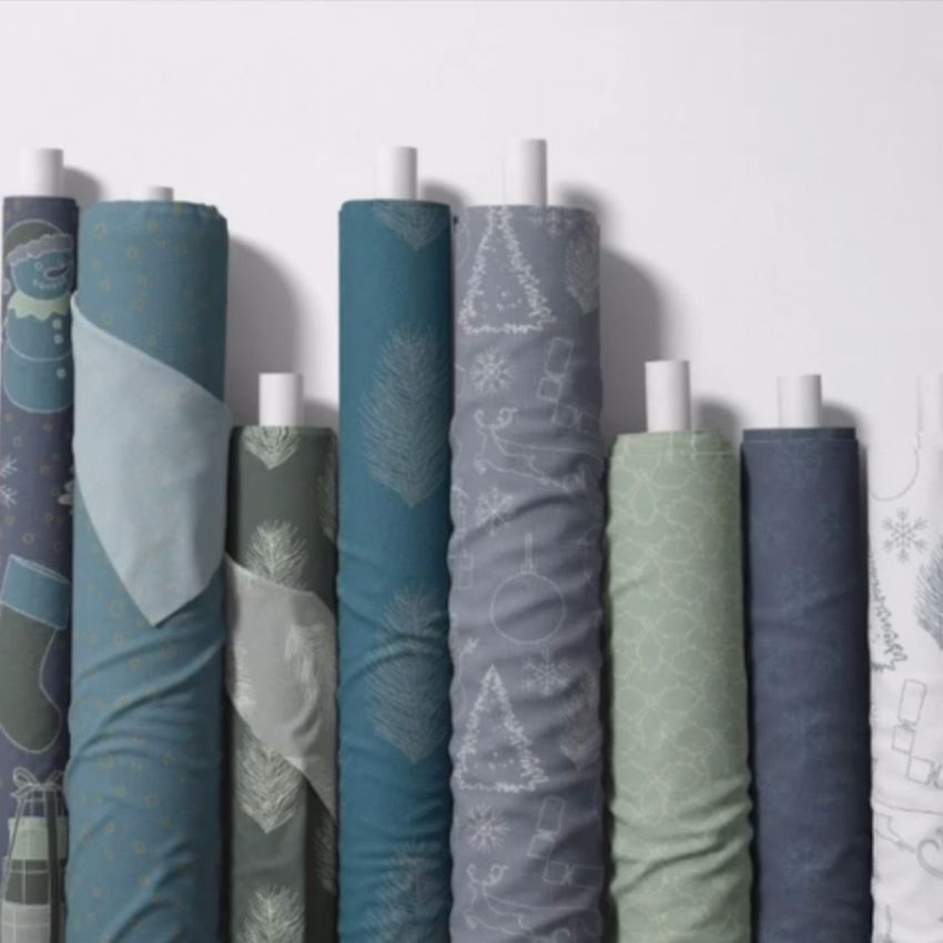 Fabric rolls mockup showing eight upright rolls with winter and Christmas-themed patterns in blue, green, and gray tones.