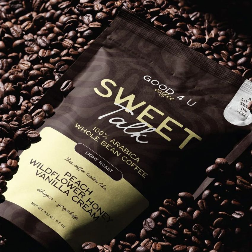 Coffee branding mockup featuring a dark coffee bag with gold and cream labels, surrounded by roasted coffee beans.
