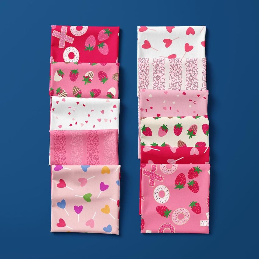 Folded fabrics mockup showing ten fabric pieces with heart, strawberry, and geometric patterns in pink, red, and white tones on a blue background.