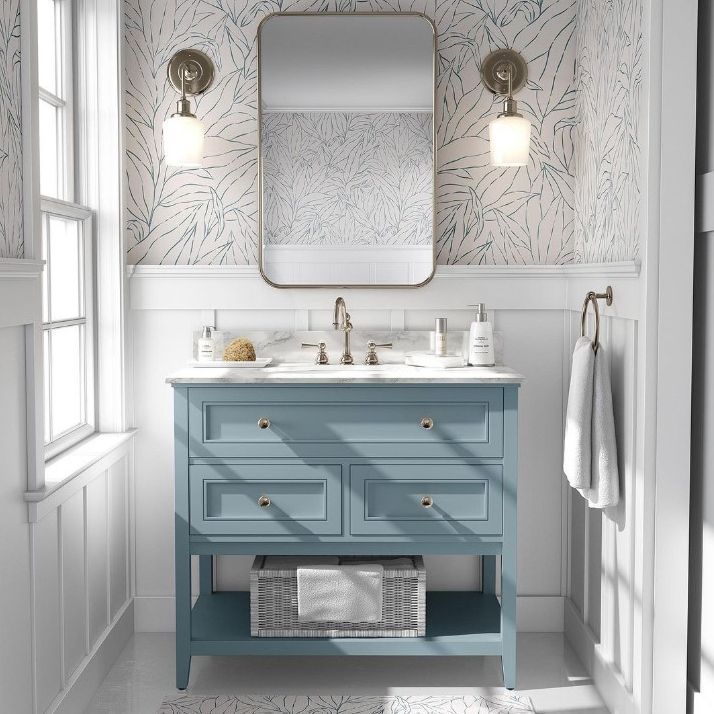 Bathroom mockup showing a blue vanity with a marble countertop, rectangular mirror, and two wall sconces on patterned wallpaper.